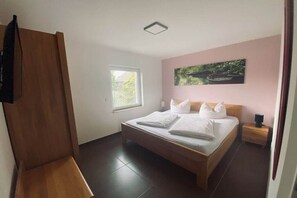 Ein Schlafzimmer mit Bett, Fenster, Gemälde und Nachttisch.