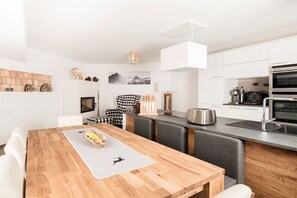 A modern kitchen with white cabinets, a wooden dining table, and a built-in island with seating. - Chalet Tubbs (4 persons) (Mauterndorf)
