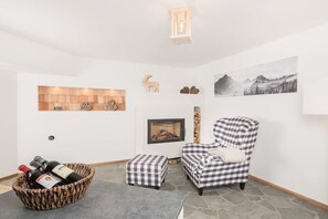 A cozy room with a fireplace, a checkered armchair, a basket of wine bottles, and a framed picture on the wall. - Chalet Tubbs (4 persons) (Mauterndorf)