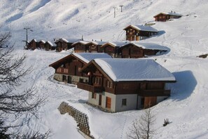 Eine schneebedeckte Berghütte mit mehreren Holzhütten, einer Seilbahn und freiem Blick auf die verschneite Landschaft.