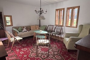 Ein Wohnzimmer mit einer Couch, Sesseln, einem Tisch, einer Chandelüster und Fenstern.