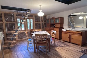 Ein Essbereich mit Tisch und Stühlen, Holzschränke, eine Küche mit Spüle und Spiegel sowie eine Treppe mit Metallgeländer.