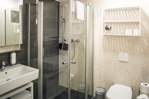 Un baño con cabina de ducha de vidrio, un lavabo blanco, un inodoro y un perchero para toallas.