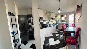 Une cuisine moderne avec un sol à carreaux noirs et blancs, des meubles blancs, un réfrigérateur noir et une table à manger avec des chaises rouges.