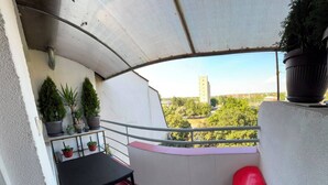 Un balcon avec une table, des chaises, des plantes en pot et une poubelle rouge.
