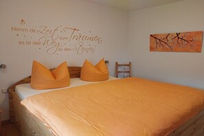 Ein Schlafzimmer mit einem Bett, orangefarbener Bettwäsche, einer Wand mit einem deutschen Schriftzug und einem Gemälde von Ästen.