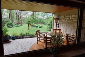 A patio with a wooden table and chairs, a stone wall, and a view of a garden. - Holiday apartment with 1 bedroom (Bad Schandau)