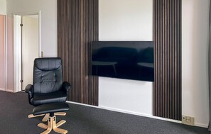 Una habitación moderna con un sillón de cuero negro, un televisor de pantalla plana montado en una pared con textura y paneles de madera verticales.