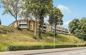 A multi-story building with balconies, situated on a grassy hill.