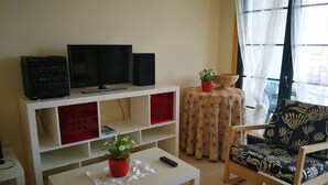 Een woonkamer met een televisie, speakers, een salontafel met een plant, een gestreept sofa en een kleine tafel met een schaal.