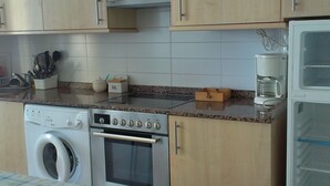 Een keuken met een wasmachine, oven, koffiezetapparaat en kasten.