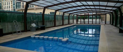 Une piscine intérieure dotée d’un toit en verre, d’une échelle et d’un banc.