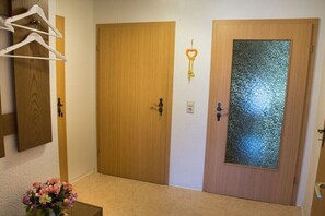 A hallway with two wooden doors, one with a frosted glass panel, a heart-shaped decoration on the wall, and a vase with flowers on the floor. - "At the castle park" (Bertsdorf-Hörnitz)