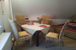 A dining area with a table set for two, wicker chairs, a vase with flowers, and a sofa in the background. - Holiday apartment with 1 bedroom (Großpösna)