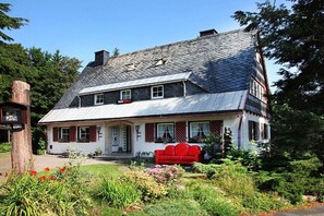 Ein zweistöckiges Haus mit geneigtem Dach und einer Veranda, auf der ein rotes Sofa steht.