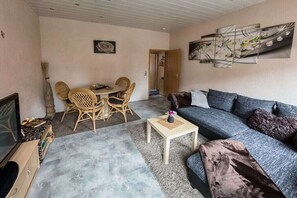 Ein Wohnzimmer mit einer Couch, einem Couchtisch, einem Esstisch mit Stühlen und einem Bild an der Wand.