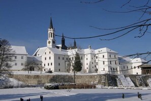 Ein großes, historisches Gebäude mit einem markanten Turm und mehreren Flügeln, umgeben von Schnee.