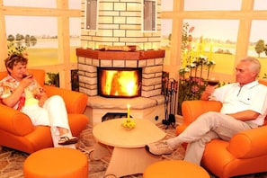 A room with a fireplace, orange seating, and a small table with a candle. - Holiday room with 1 bedroom (Märkische Heide OT Biebersdorf)