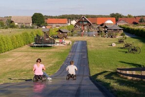 A rural setting with a paved path, wooden structures, and a large building with a red roof. - Holiday room with 1 bedroom (Märkische Heide OT Biebersdorf)