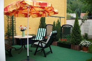 Eine Terrasse mit zwei Stühlen, einem Tisch und einem Sonnenschirm.