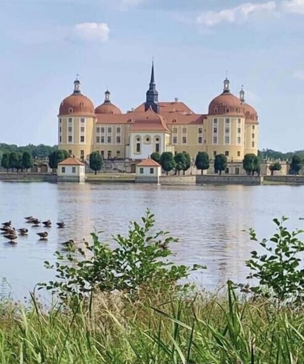 Ein großes, historisches Gebäude mit mehreren Kuppeln und einem markanten Turm, gelegen an einem ruhigen Gewässer.