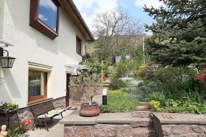 Ein Haus mit einem Kiesweg, einer Bank, einem Blumentopf und einem Garten mit verschiedenen Pflanzen und Blumen.
