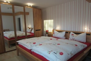 A bedroom with a large mirror, a bed with floral bedding, a wooden headboard, and a striped wall. - Holiday apartment with 2 bedrooms (Meißen)