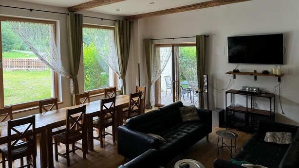Una sala de estar con comedor, vigas de madera, televisor y un ventanal grande.