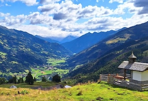 A mountainous landscape with a small wooden cabin on a grassy hill.