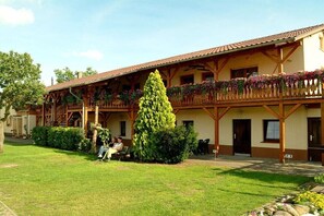 Ein traditionelles Chalet mit überdachter Terrasse, einem gepflegten Rasen und einem kleinen Baum in der Mitte.