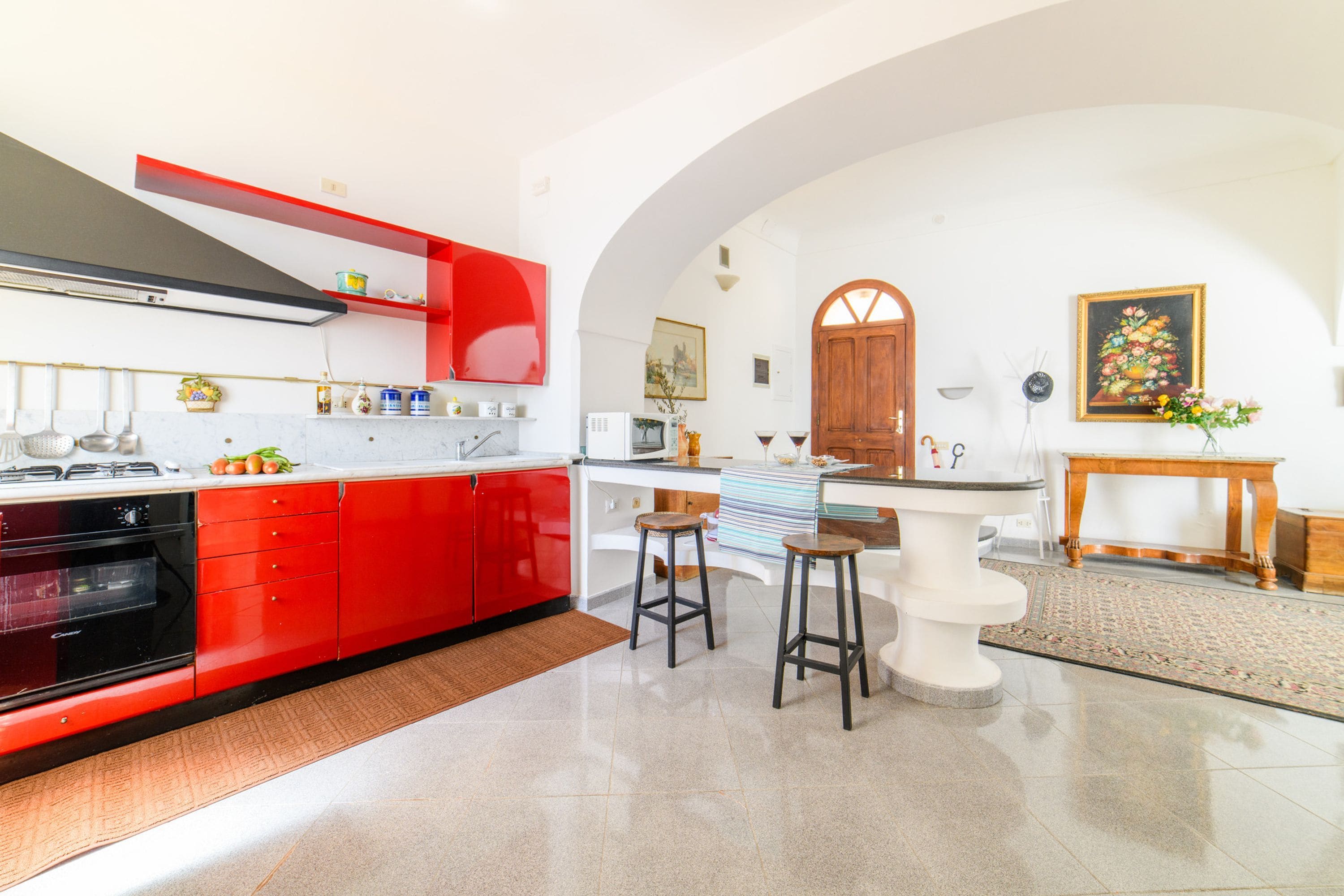 A modern kitchen with red cabinetry, a white countertop, and a bar area with stools.