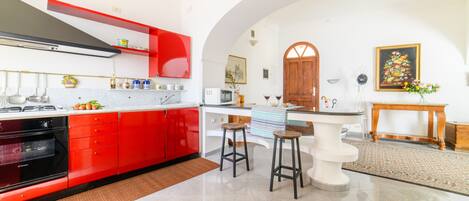 A modern kitchen with red cabinetry, a white countertop, and a bar area with stools.
