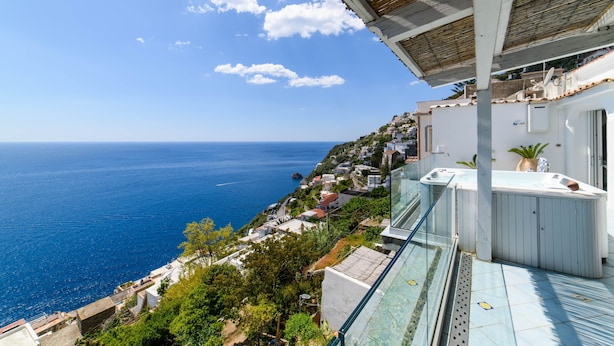 Un balcón con barandilla de cristal que ofrece vistas a un pueblo costero y al mar.