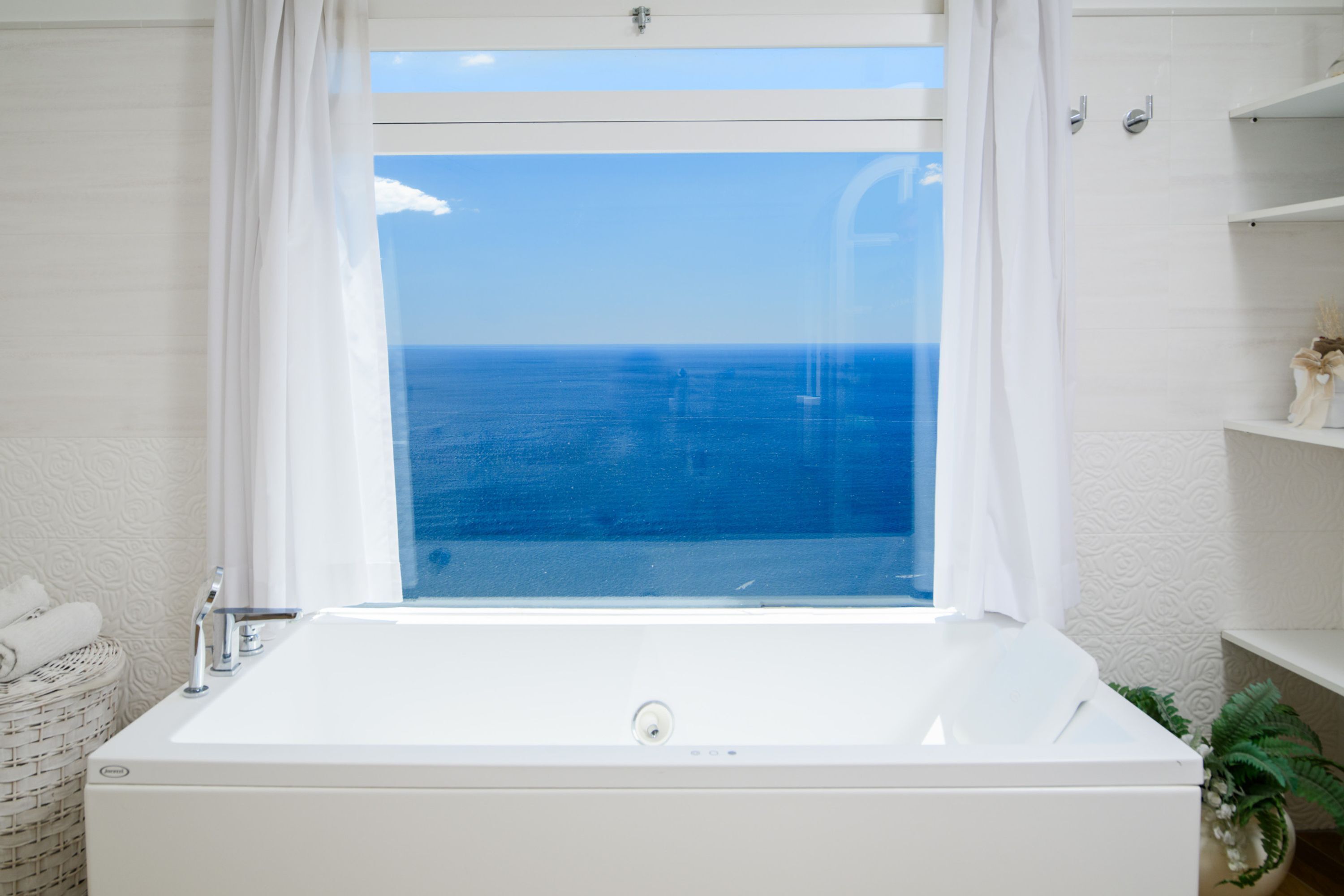 Ein Badezimmer mit einer Badewanne, einem Fenster mit Meerblick und einem Regal mit einer Pflanze.