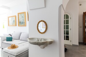 A modern living room with a sofa, a laptop, a wall-mounted sink, and framed artwork. - Estate4home - Villa Lettieri (Praiano)