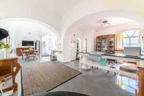 A spacious living area with a dining table, a large rug, and a kitchen area with modern appliances. - Estate4home - Villa Lettieri (Praiano)