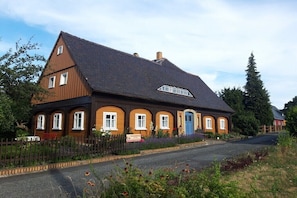 Ein zweigeschossiges Gebäude mit Satteldach, zahlreichen Fenstern und einer blauen Tür.