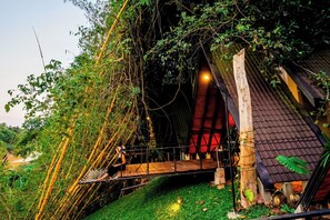 A rustic wooden structure with a sloped roof, surrounded by dense foliage and a small wooden bridge. - Taro Resort (Otharawadiya)