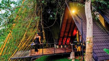 A treehouse with a wooden platform, netted climbing area, and a red-roofed structure.