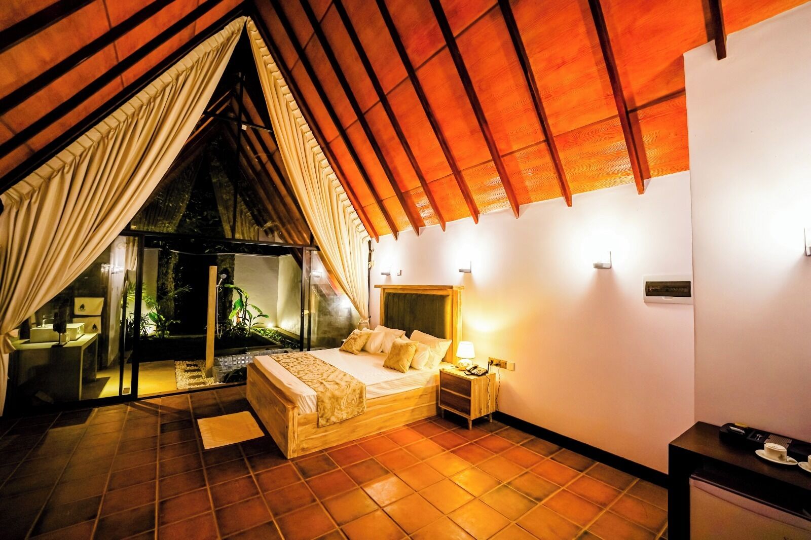 A bedroom with a bed, bedside table, and a view of a garden through a glass door.