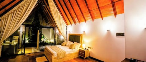Un dormitorio con cama, mesita de noche y vistas a un jardín a través de una puerta de vidrio.
