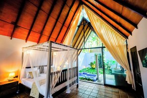 A room with a four-poster bed, a nightstand, and a view of a garden through a large window. - Taro Resort (Otharawadiya)