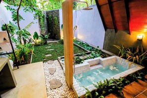 Un área de piscina pequeña al aire libre con un sendero de piedra, rodeada de vegetación y una estructura de madera.