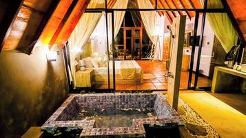 A cozy bedroom with a large bed, a glass door leading to a bathroom, and a small hot tub area.