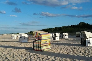 Strandhütten mit einem markanten Streifenmuster, anreihum auf einem Sandstrand bei blauem Himmel.