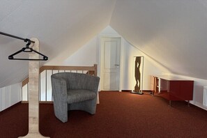 Ein Zimmer mit schrägem Dach, einem Holzstuhl, einem roten Schrank und einer Hängeleuchte.