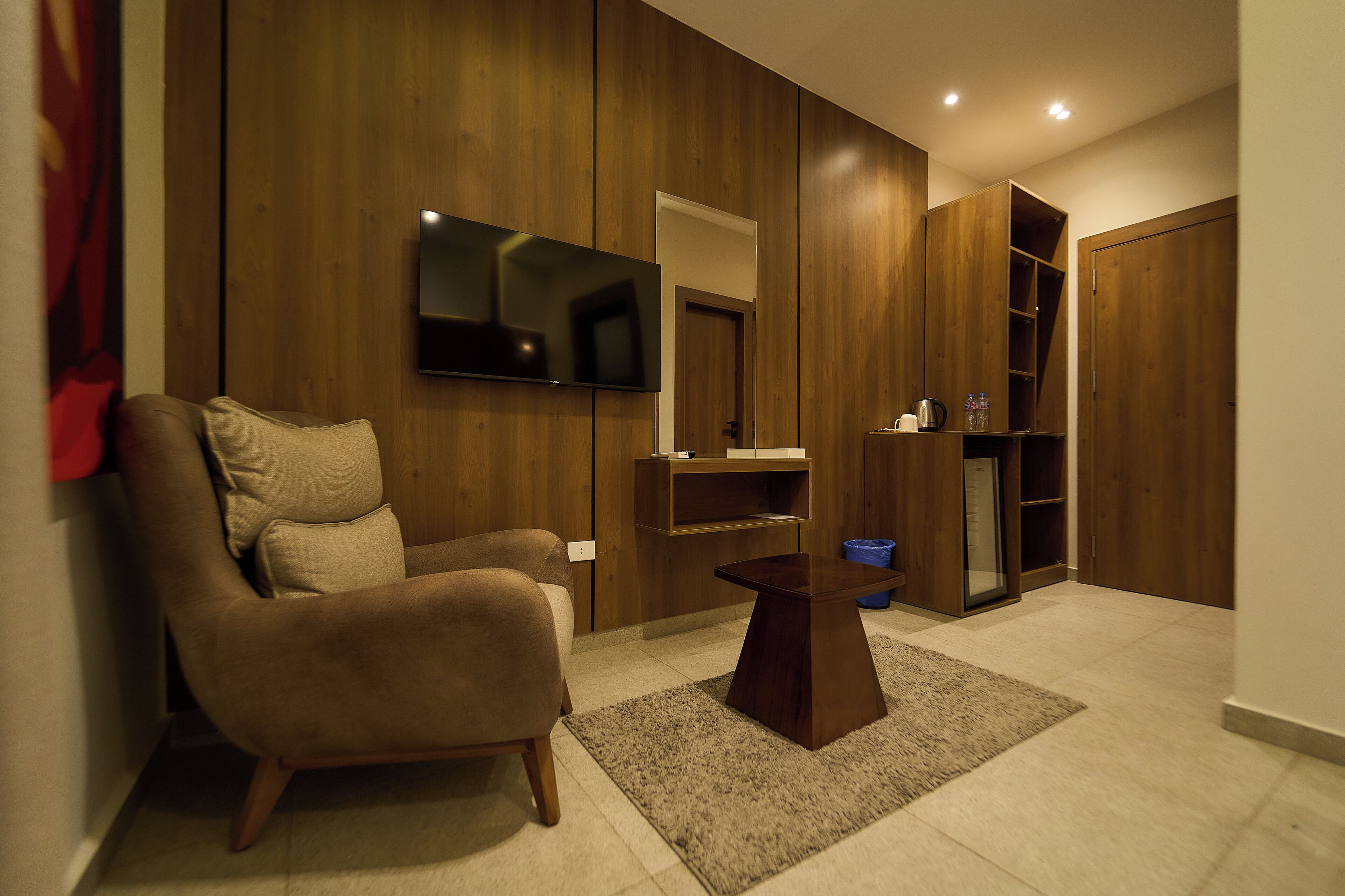 A modern living room with a sofa, a coffee table, a flat-screen TV mounted on the wall, and a wooden wardrobe.