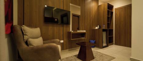 A modern living room with a sofa, a coffee table, a flat-screen TV mounted on the wall, and a wooden wardrobe.