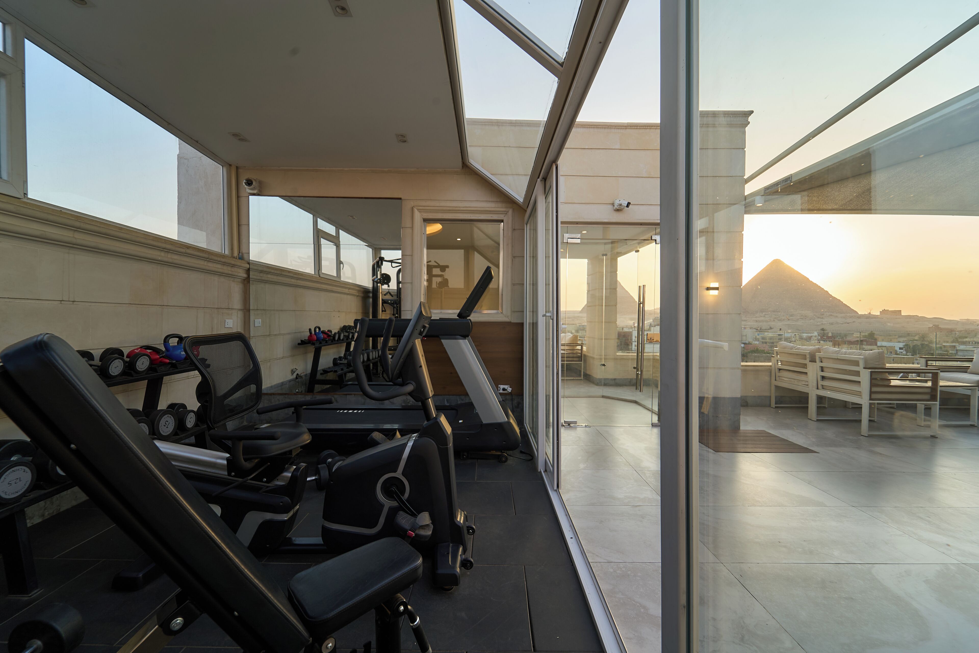 Ein Fitnessstudio mit Trainingsgeräten und Blick auf einen Berg bei Sonnenuntergang.