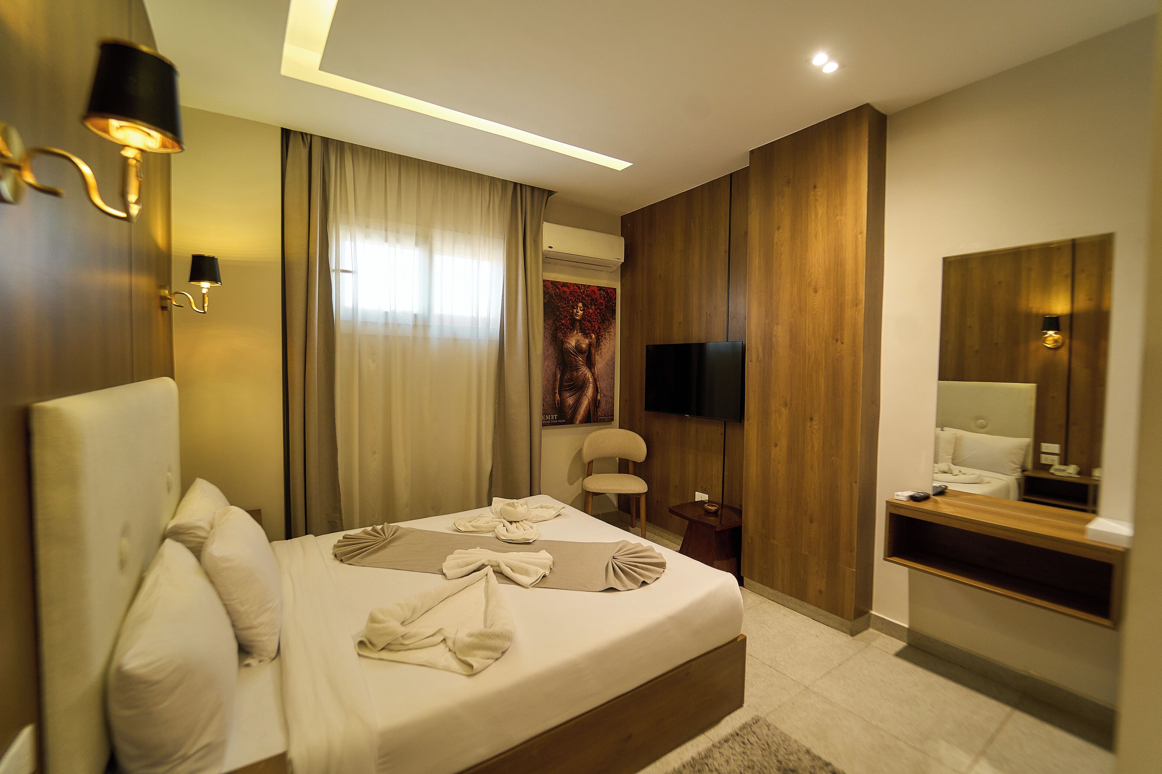 A hotel room with a large bed, a flat-screen TV, a wooden wardrobe, and a bathroom with a mirror.